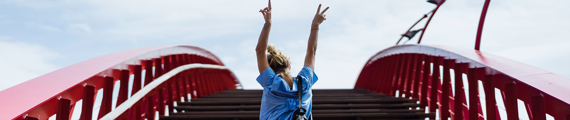 woman with arms raised in celebration at the top of an arched walkway bridge