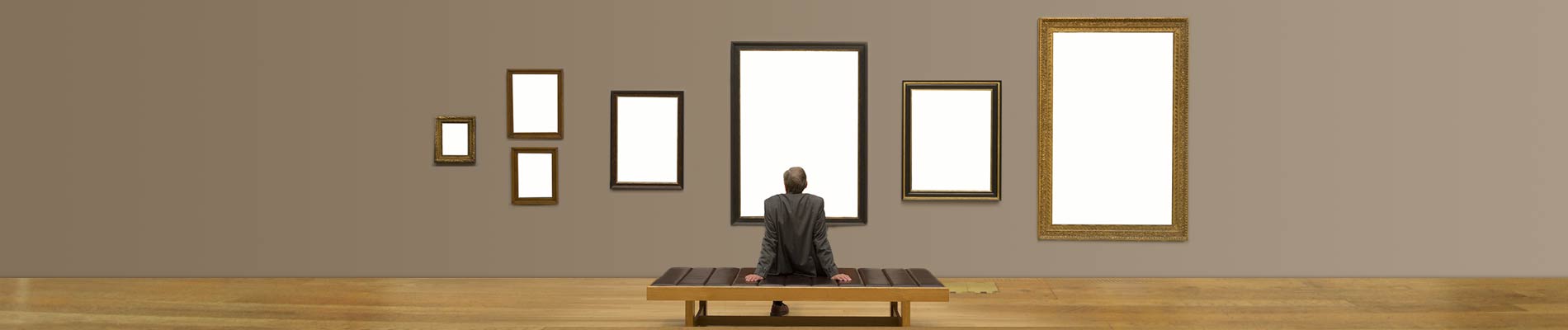 A man sitting on a bench within a room with seven blank picture frames