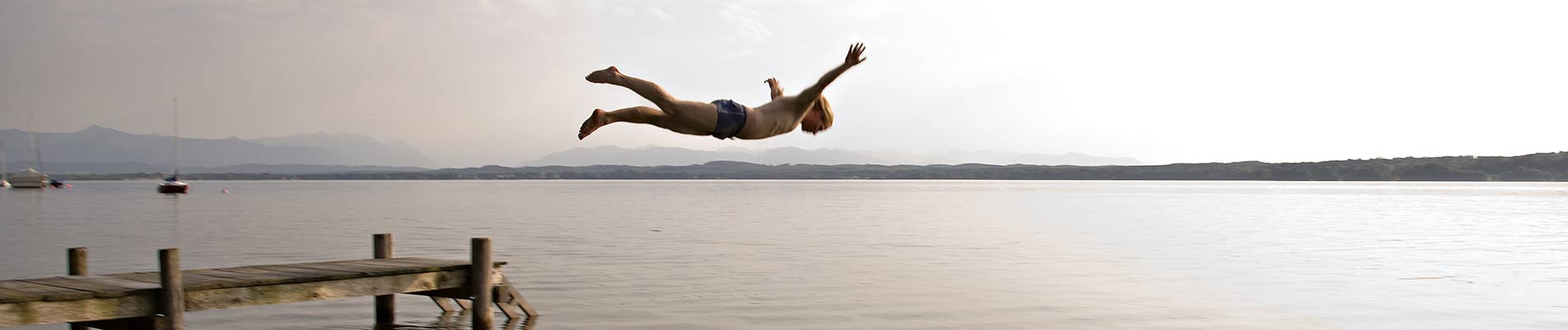 A young man diving off of a dock into a lake