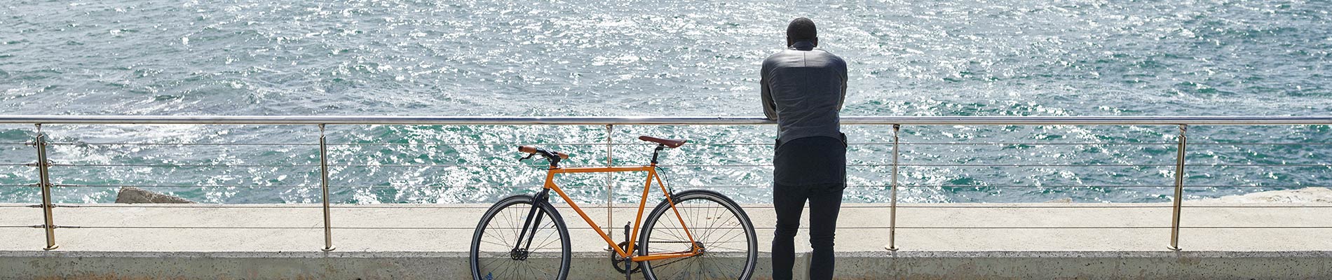 A man standing near his bike at a railing overlooking a body of water