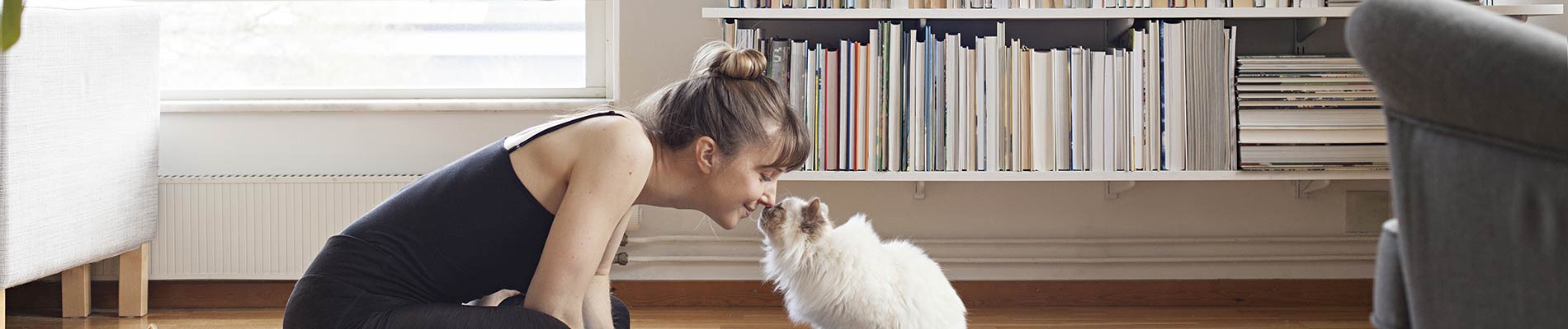A woman sitting on the floor touching noses with a white cat