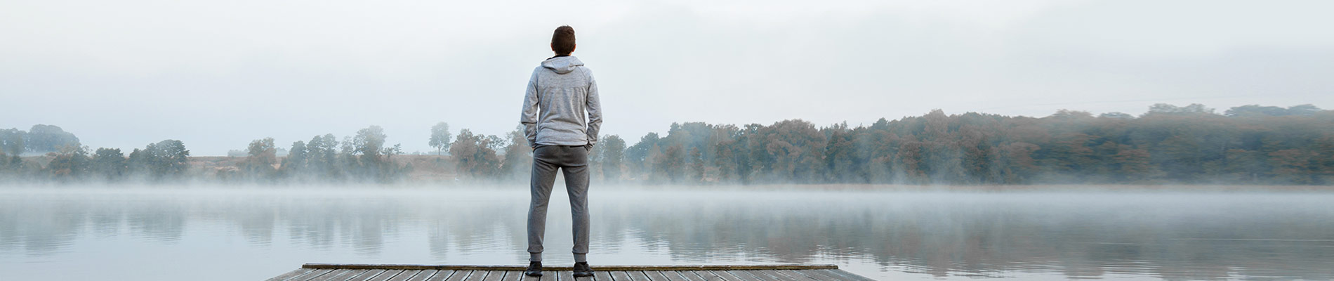 A young man standing on a dock looing over a lake with steam rising