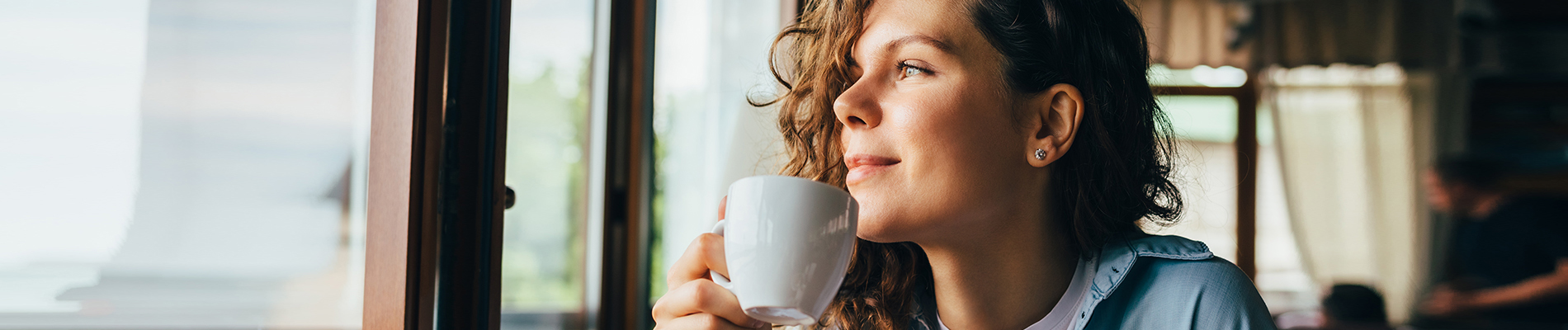 Young woman holding a cup of coffee looking out a window