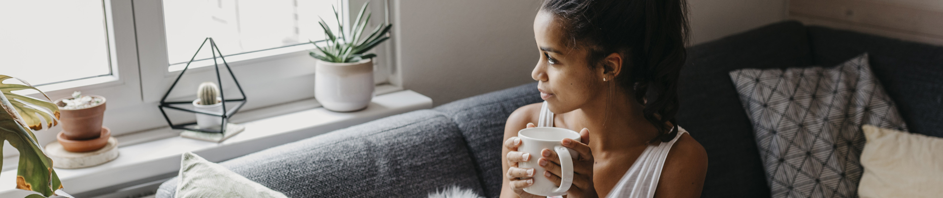Woman gazing out window on couch with a cup of coffee