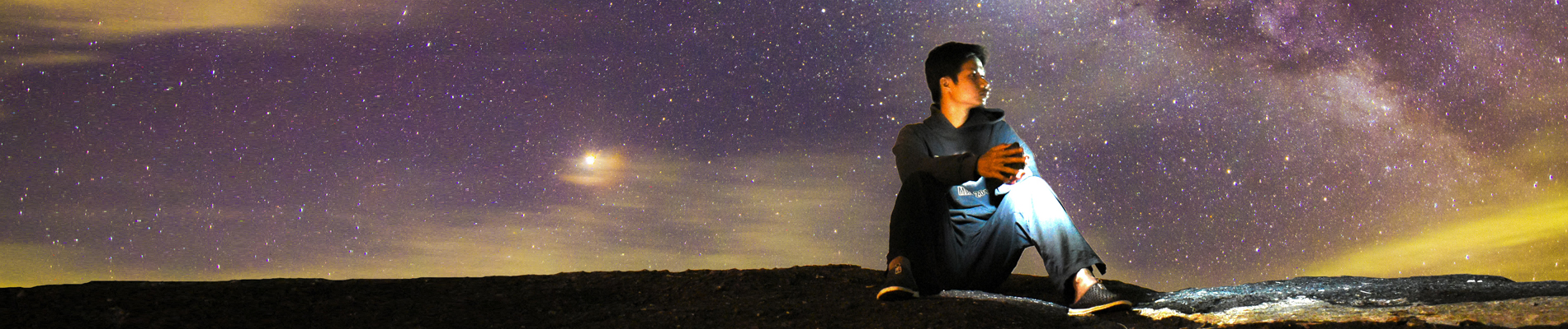 Young man sitting on the ground under the night sky